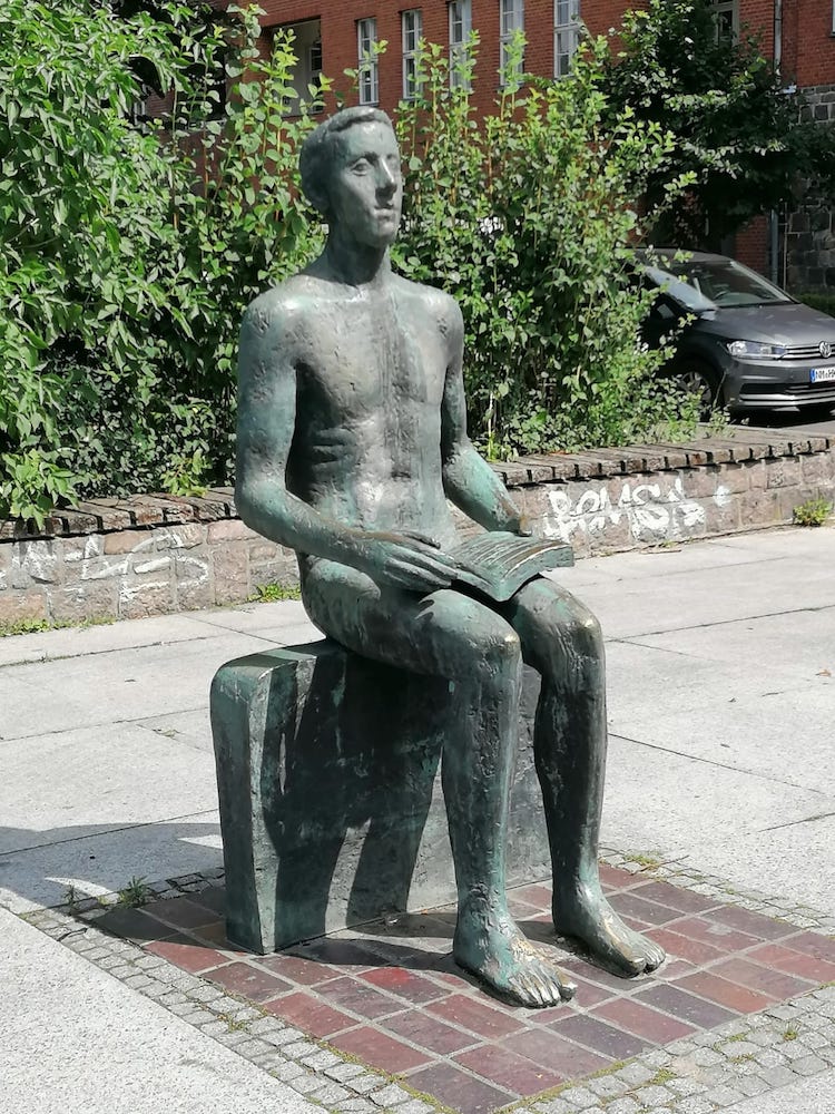 Praktische Philosophie: Kunstfigur im öffentlichen Raum, nackt sitzend und Buch haltend dargestellt, blickt kurz sinnierend auf